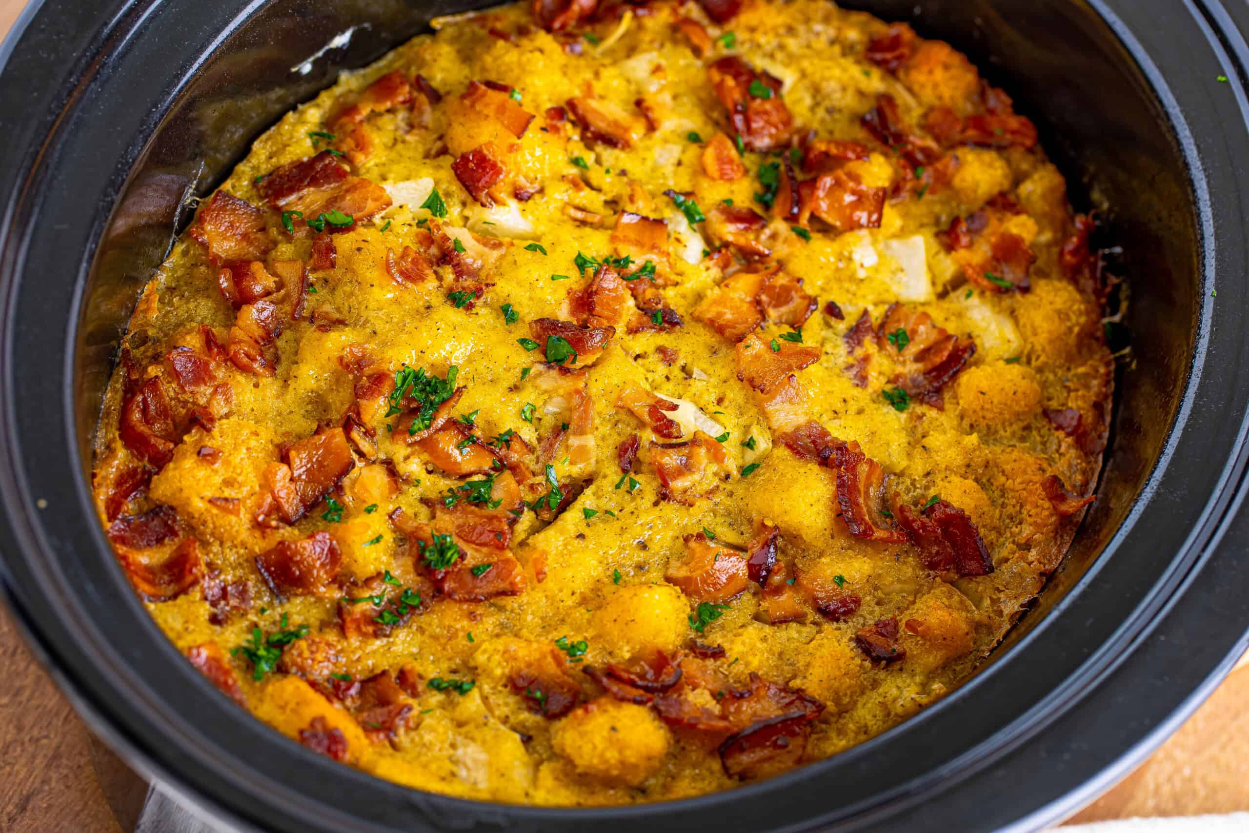 A casserole dish containing golden-brown baked contents topped with chopped herbs and crispy bits.