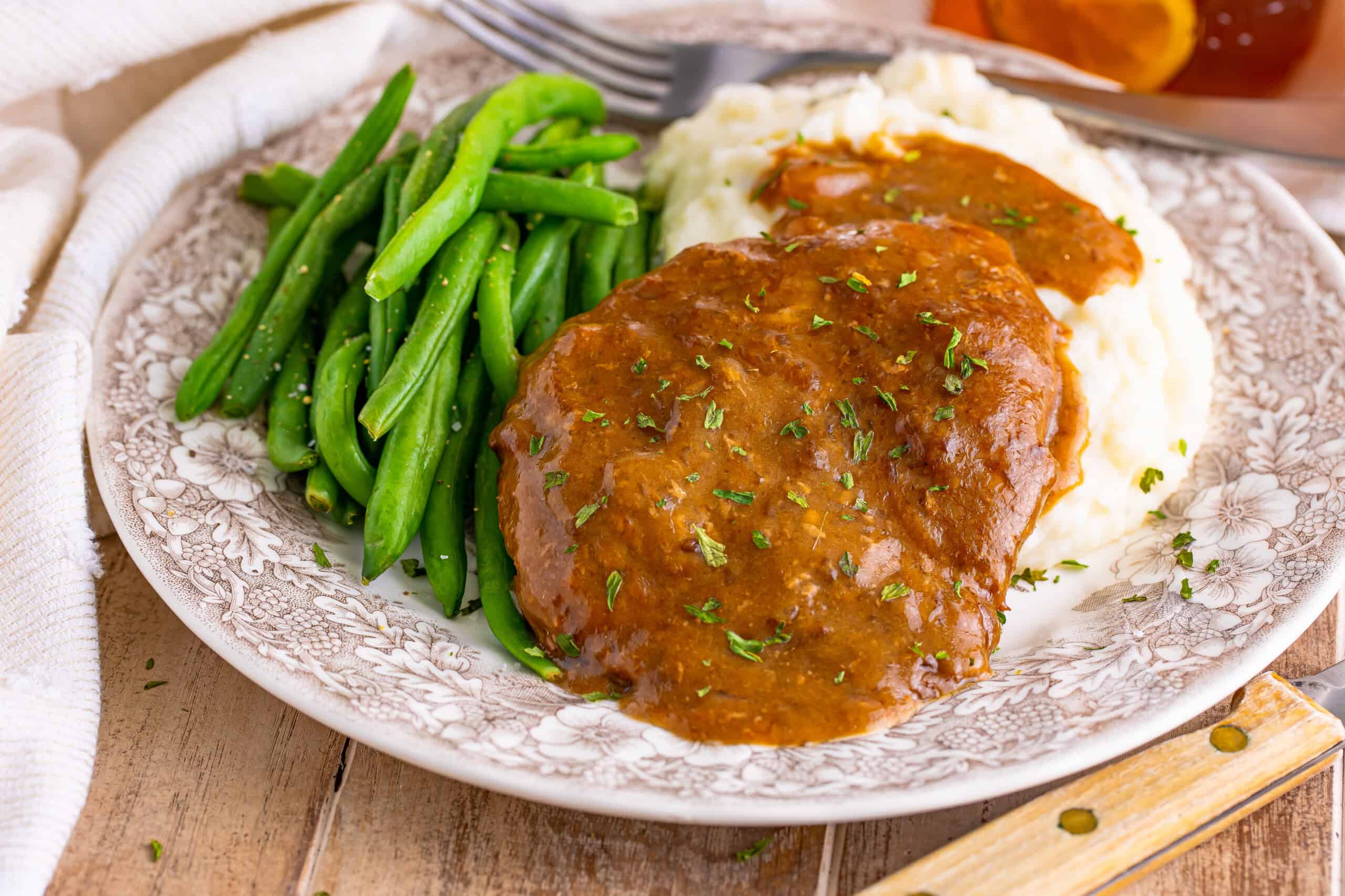 The image shows a plate containing Salisbury steak with gravy, mashed potatoes, and green beans.