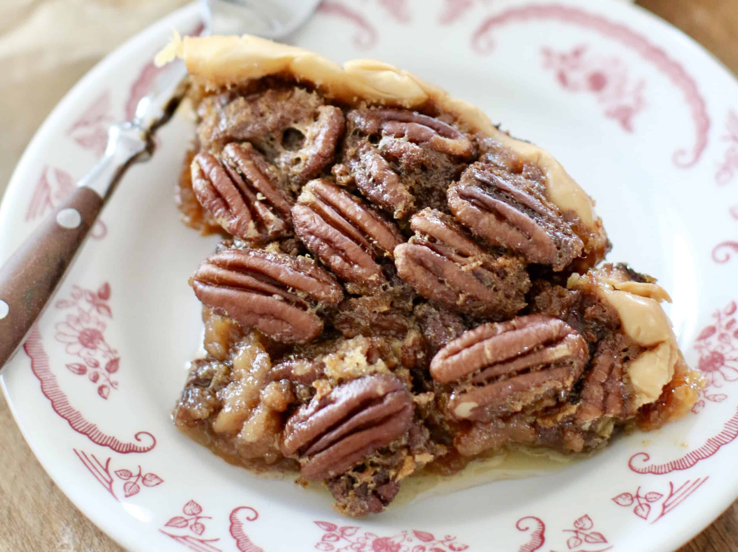 A slice of pecan pie on a patterned plate with a brown-handled fork nearby.