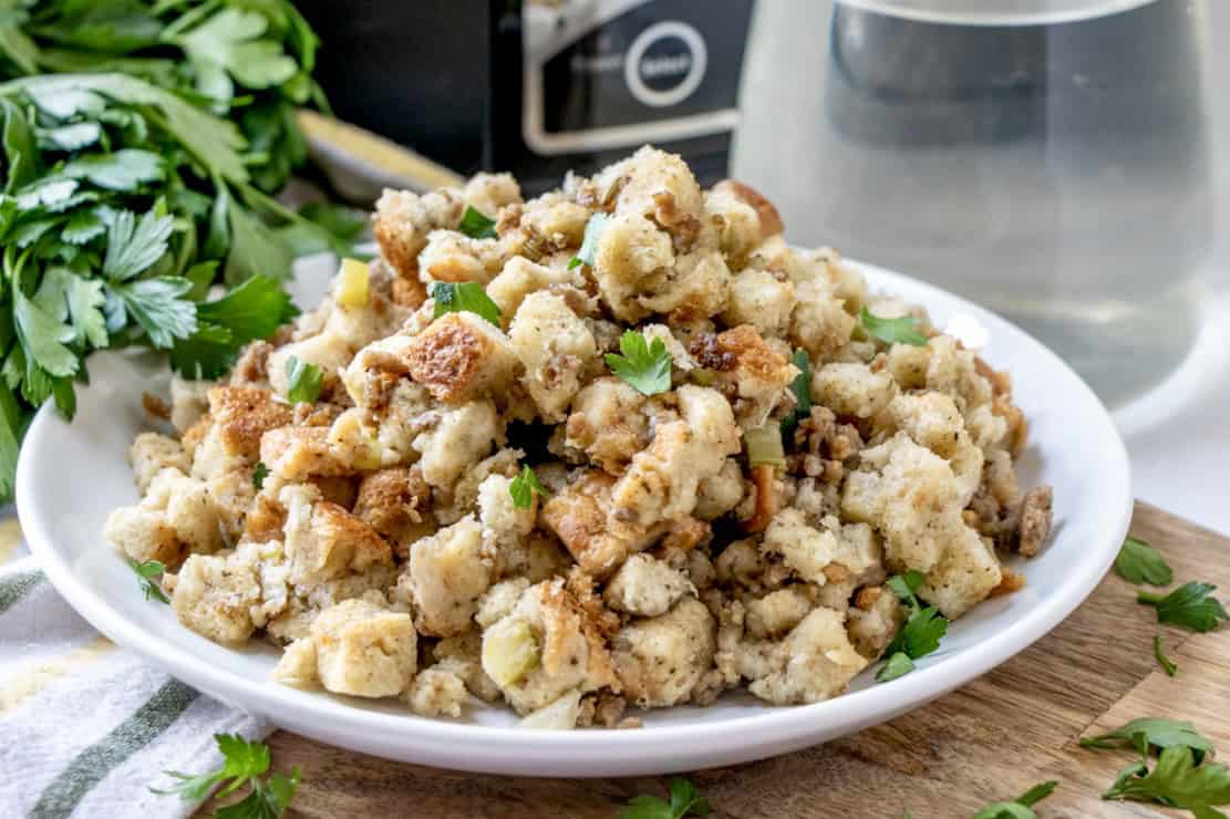 A plate of seasoned bread stuffing garnished with parsley, accompanied by a glass of water and fresh parsley.