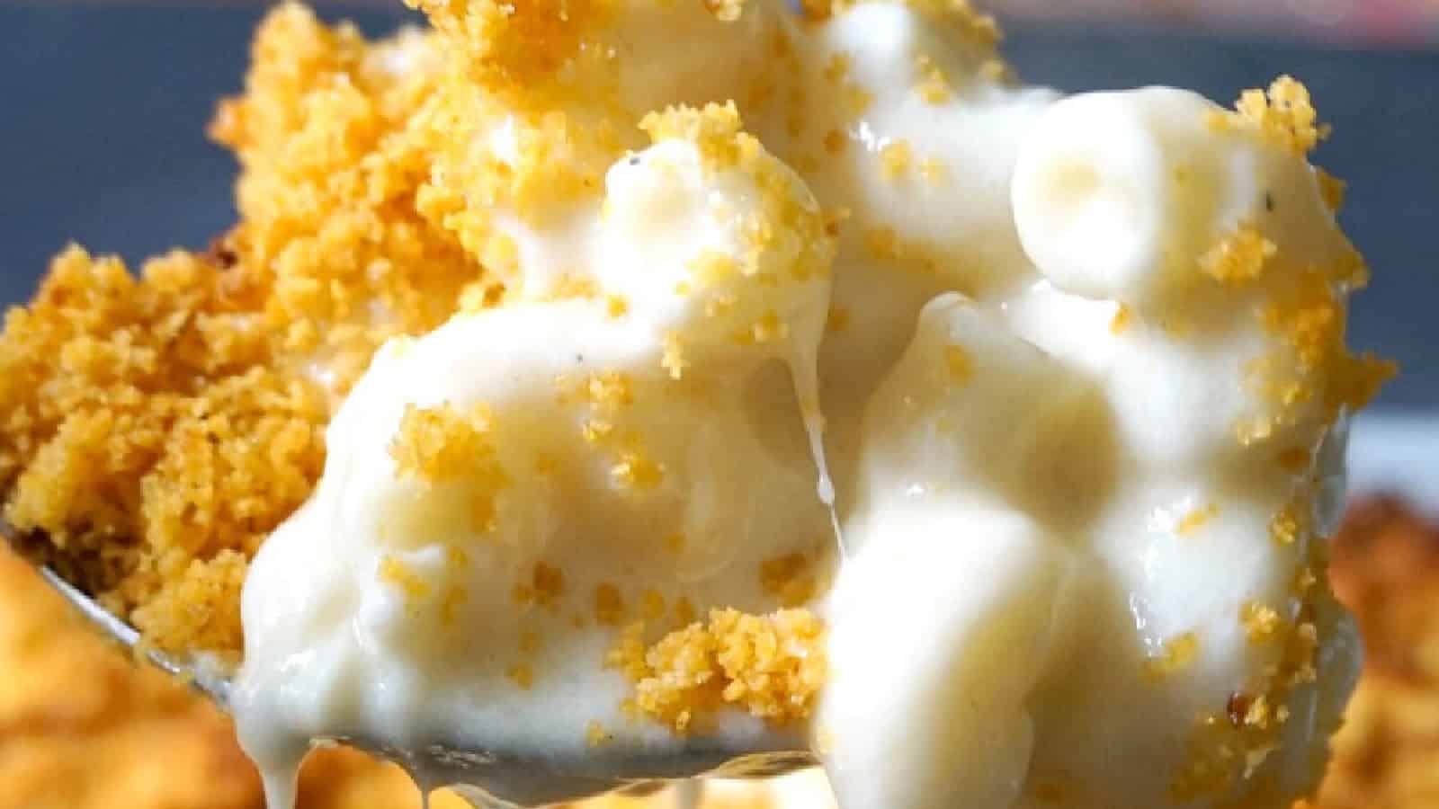 Close-up of a spoonful of creamy macaroni and cheese topped with golden breadcrumbs. The cheese sauce is thick and gooey, blending with the crispy breadcrumb topping for a rich, comforting dish.