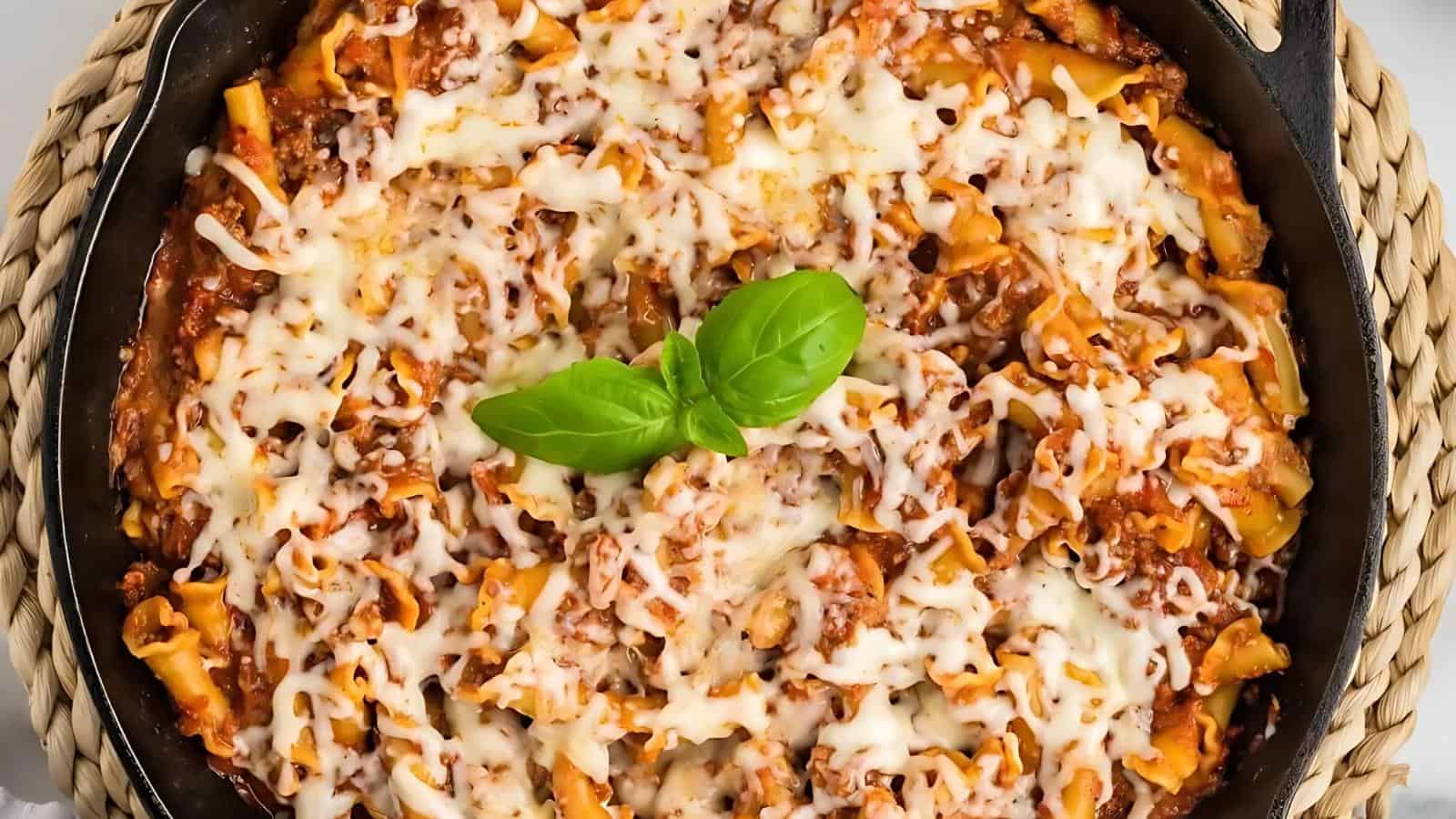 A skillet containing baked pasta with melted cheese, garnished with a basil leaf.
