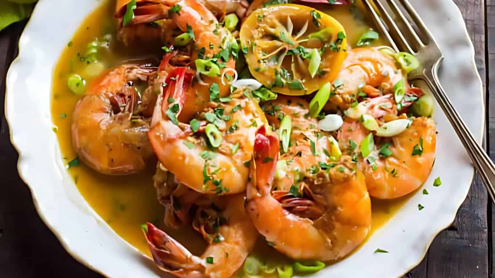 A plate with cooked shrimp in a lemony sauce, garnished with sliced green onions and herbs, with a fork resting on the side.