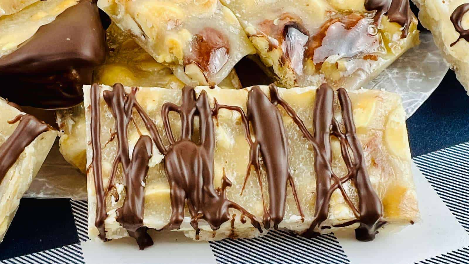 Chocolate-drizzled nut and caramel bars placed on a black and white checkered surface.
