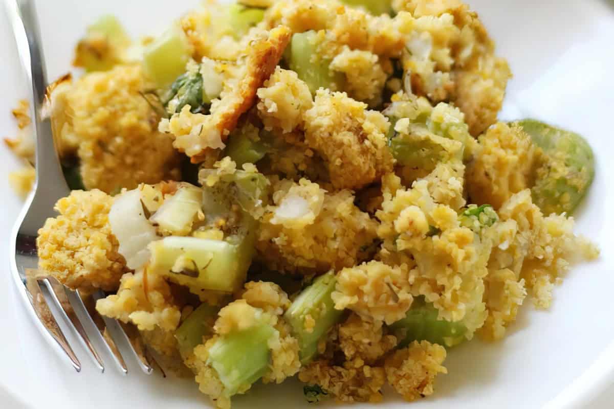 A fork next to a plate of cornbread stuffing with celery and herbs.