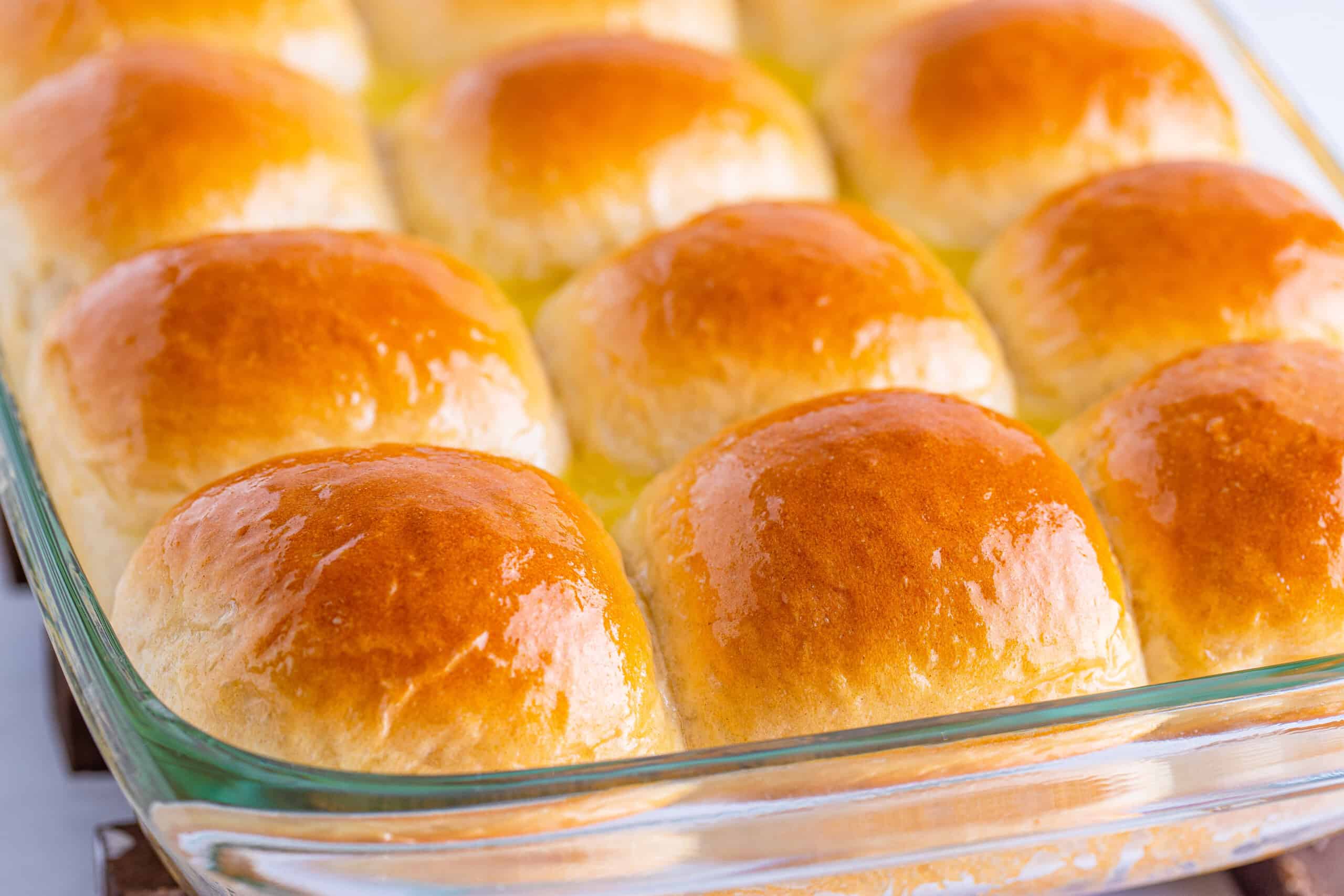 A baking dish containing twelve golden brown dinner rolls, organized in rows of three and columns of four.