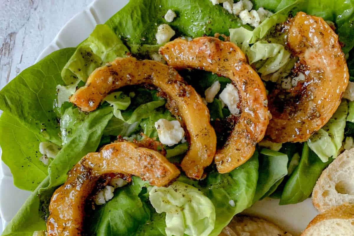 The image shows roasted squash slices, blue cheese crumbles, and leafy greens arranged on a white plate.