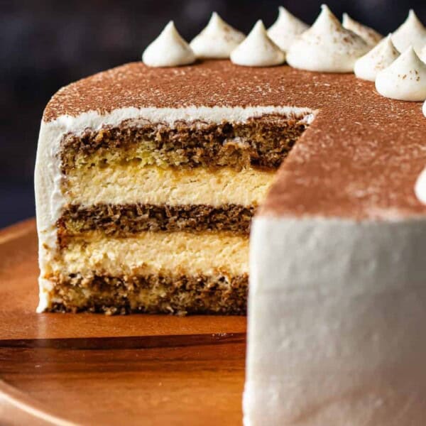A sliced espresso layer cake with cream frosting on a wooden plate, topped with whipped cream dollops.
