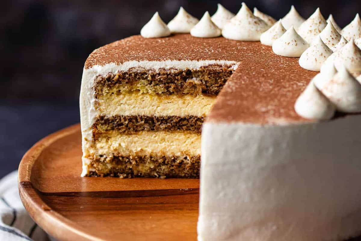 A sliced espresso layer cake with cream frosting on a wooden plate, topped with whipped cream dollops.