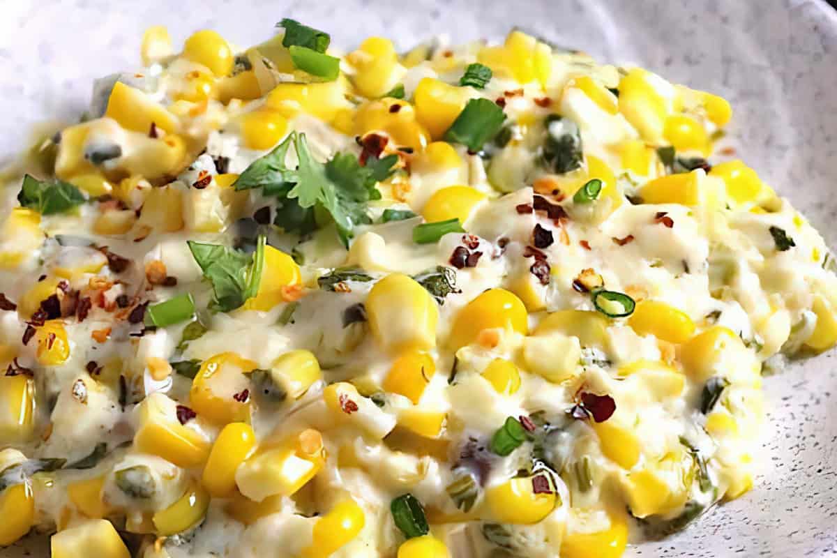 A plate of corn salad garnished with green onions, cilantro, and red pepper flakes.