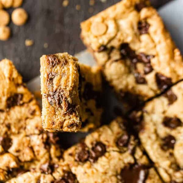 Close-up of chocolate chip and butterscotch blondie bars on a dark surface, with one bar upright and baking chips scattered nearby.