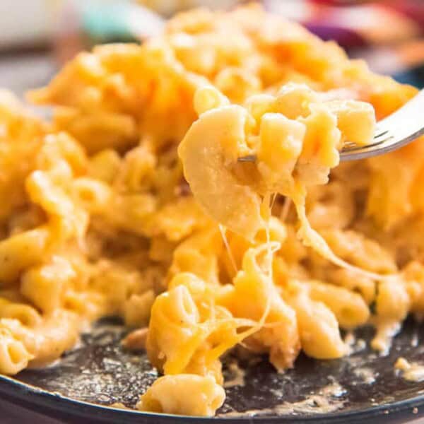 A close-up of baked macaroni and cheese on a dark plate, with a fork lifting up a cheesy portion.