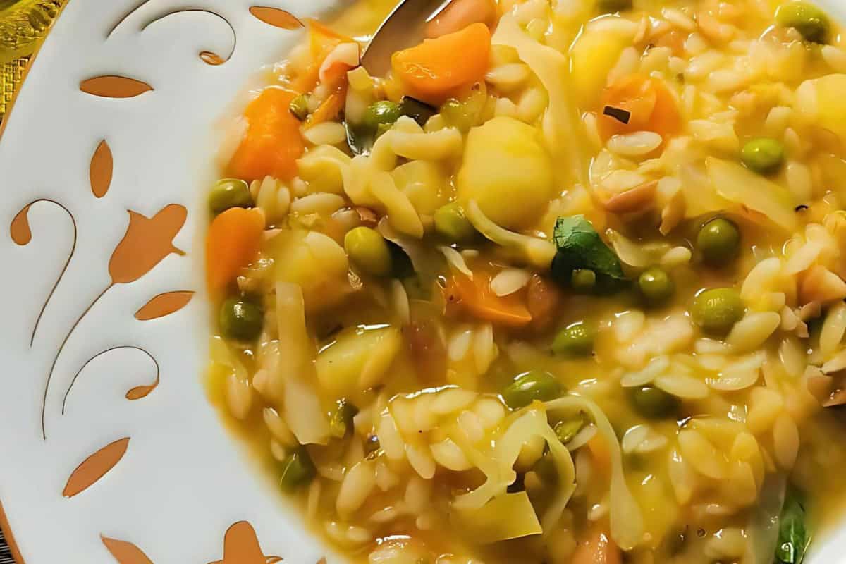 A close-up of a plate of vegetable risotto featuring peas, carrots, and potatoes in a creamy sauce. The dish is served on a white plate with a decorative pattern, with a spoon visible in the risotto.