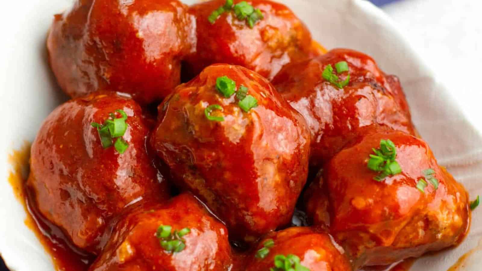 A white bowl containing glazed meatballs topped with chopped green herbs.