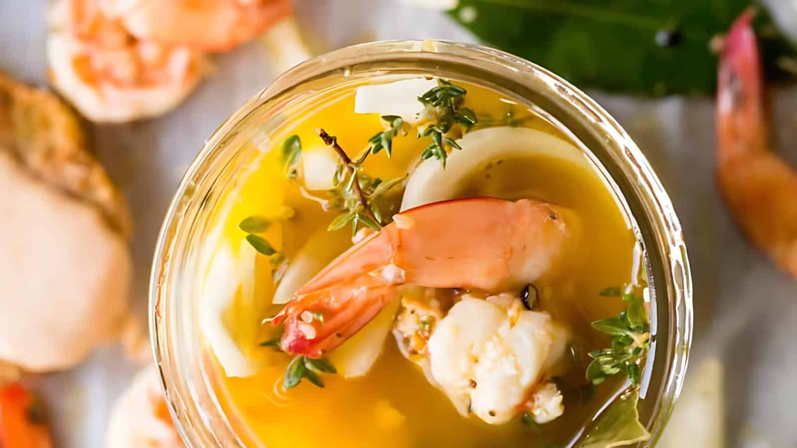 The image shows an overhead view of a glass containing shrimp, herbs, and sauce. Surrounding the glass are additional shrimp placed on the table.