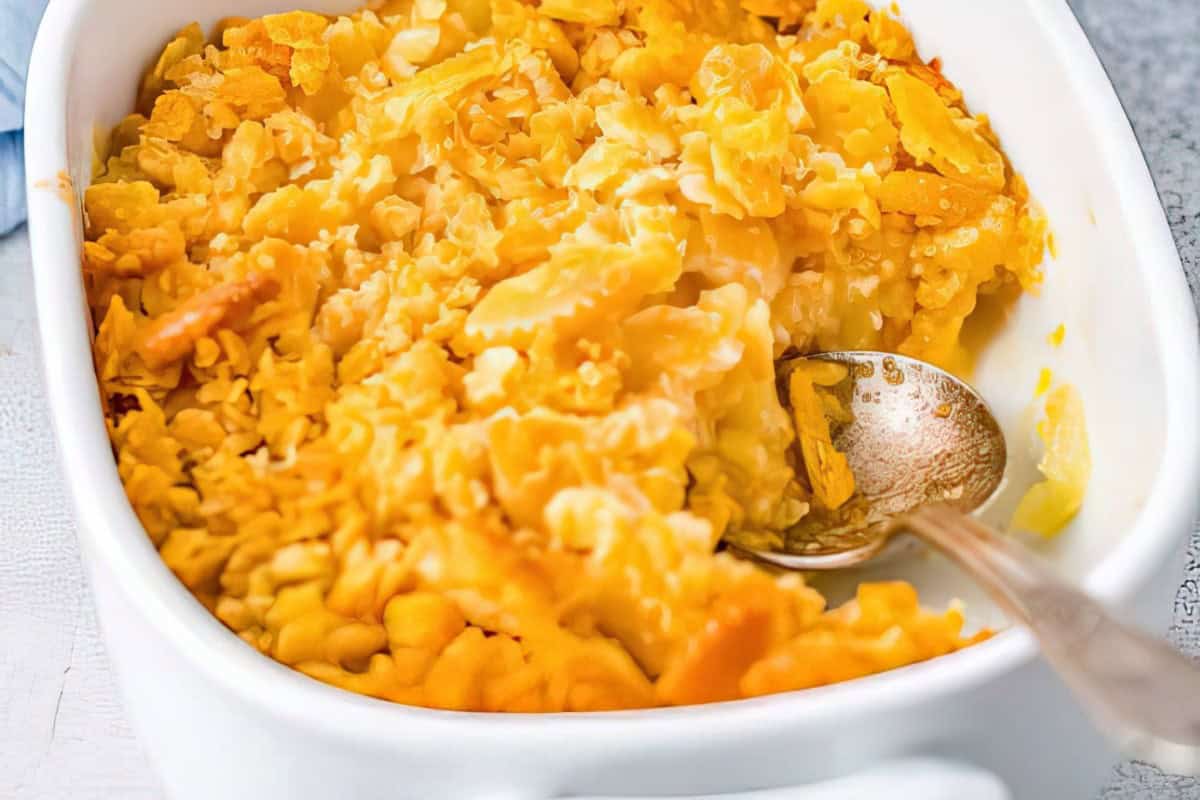A close-up of a casserole dish filled with macaroni and cheese, topped with a golden, crispy crust. A spoon is placed in the dish.
