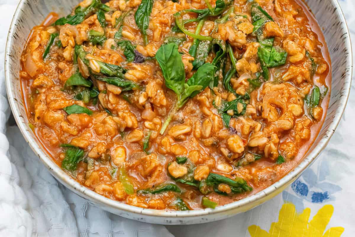 A bowl of risotto with spinach leaves in a tomato-based sauce, on a patterned cloth.