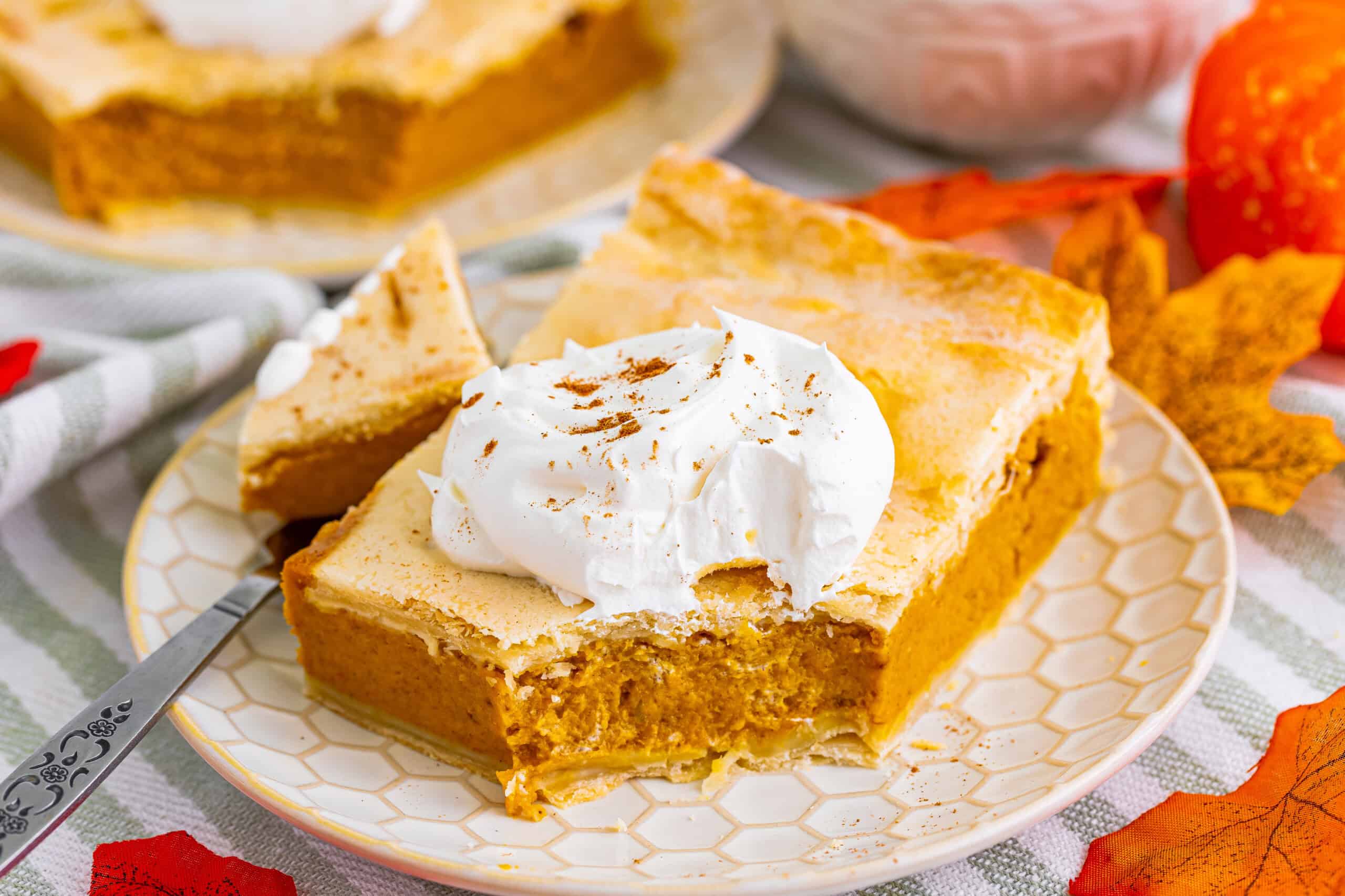 A slice of pumpkin pie on a plate topped with whipped cream, with a fork beside it. A bite is missing from the slice.