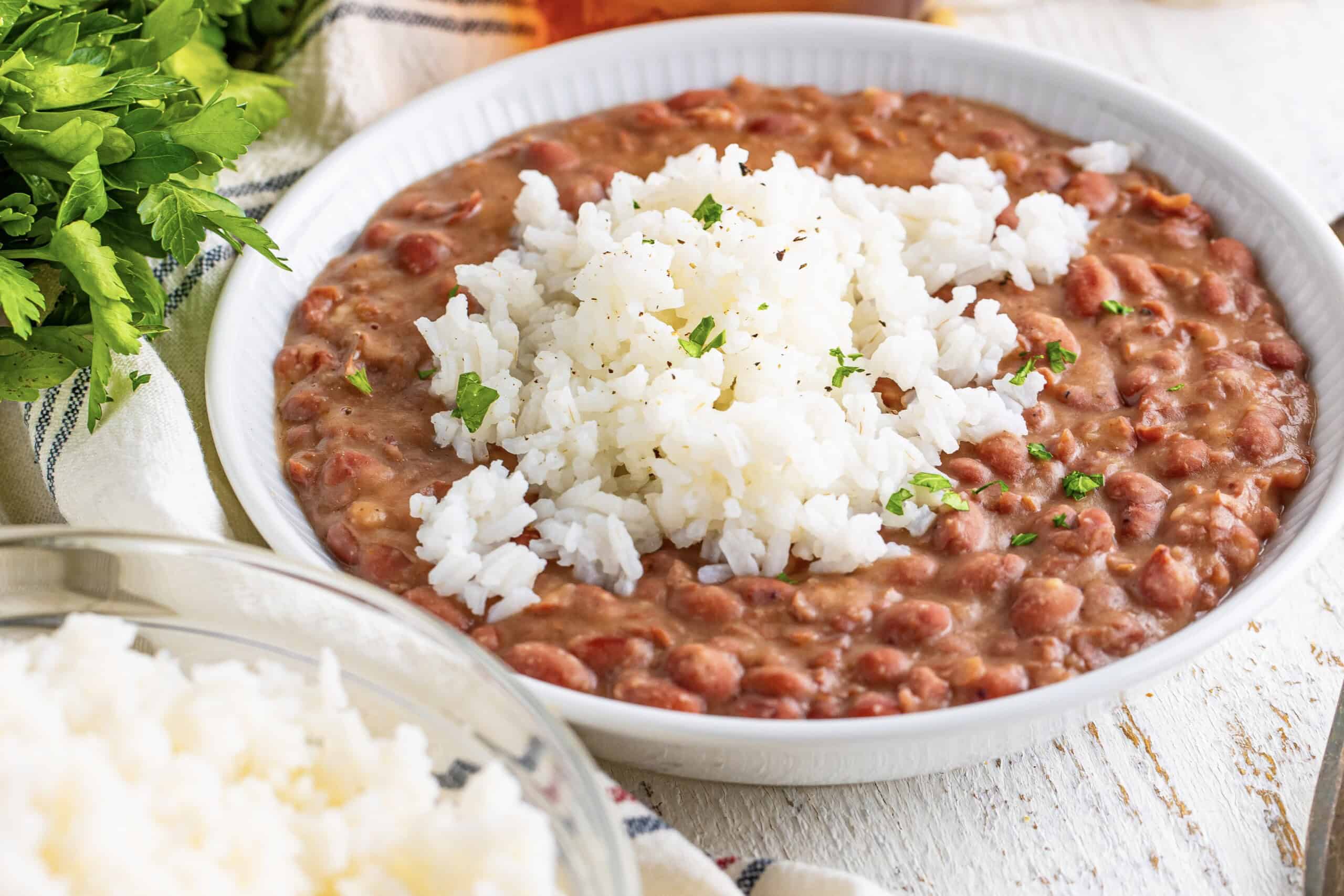 The image shows a bowl containing red beans, a scoop of white rice on top, and a garnish of chopped herbs.