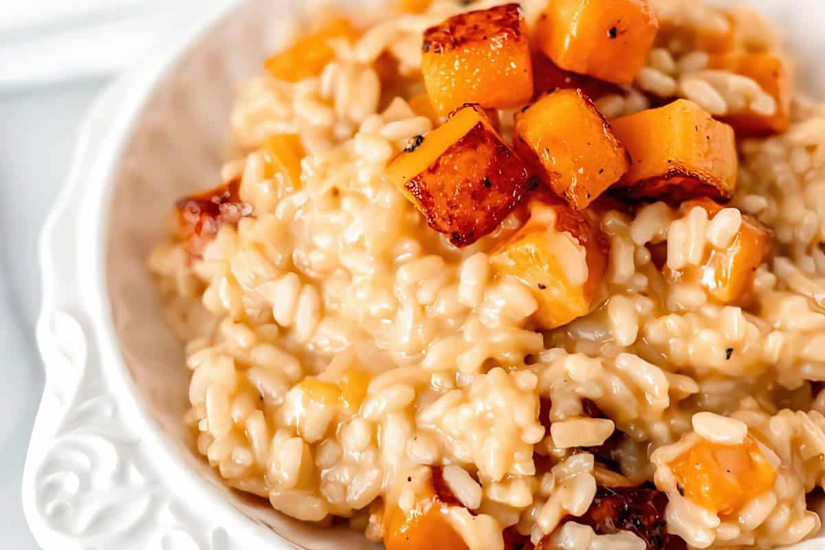 A white bowl containing creamy risotto topped with roasted cubes of butternut squash.