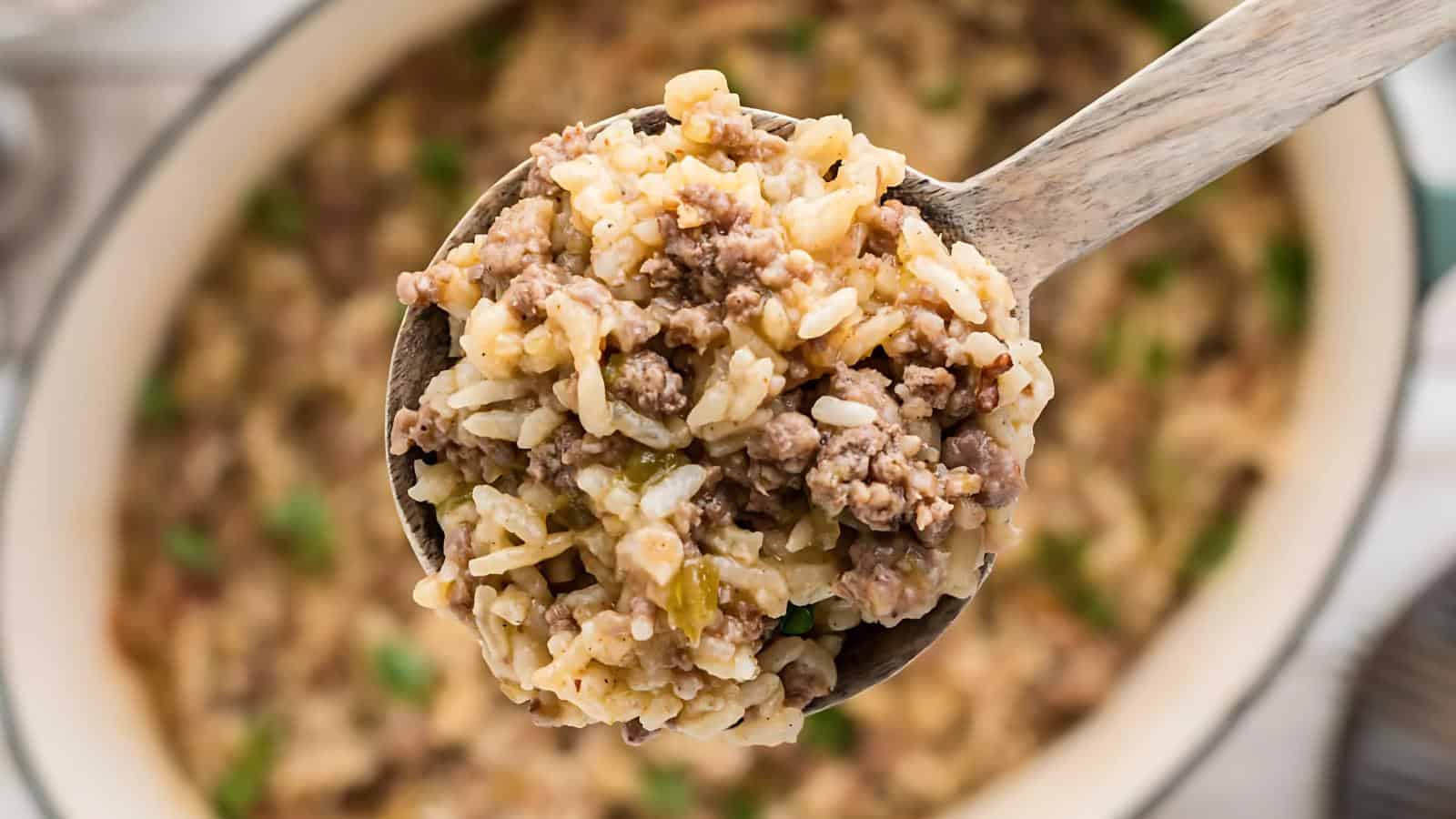 A ladle holding a mixture of rice and ground beef, with the same dish visible in the pot in the background.