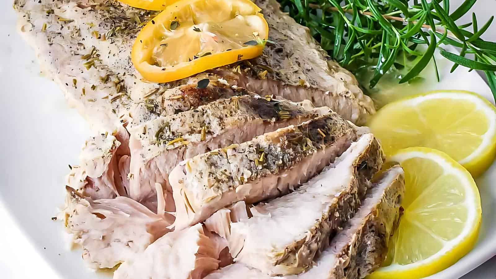 Sliced pork tenderloin garnished with lemon slices and sprigs of rosemary on a white plate.