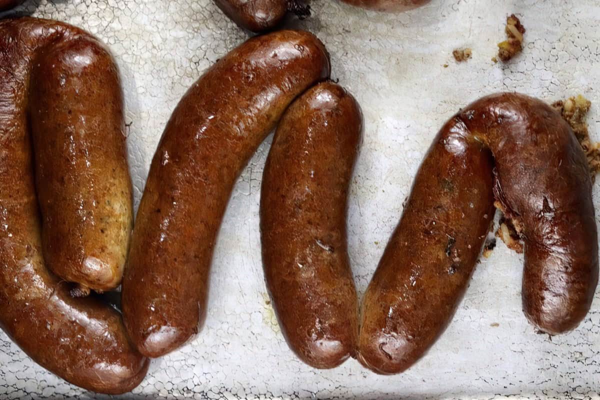 A metal baking tray with a cracked, seasoned surface containing cooked sausages.