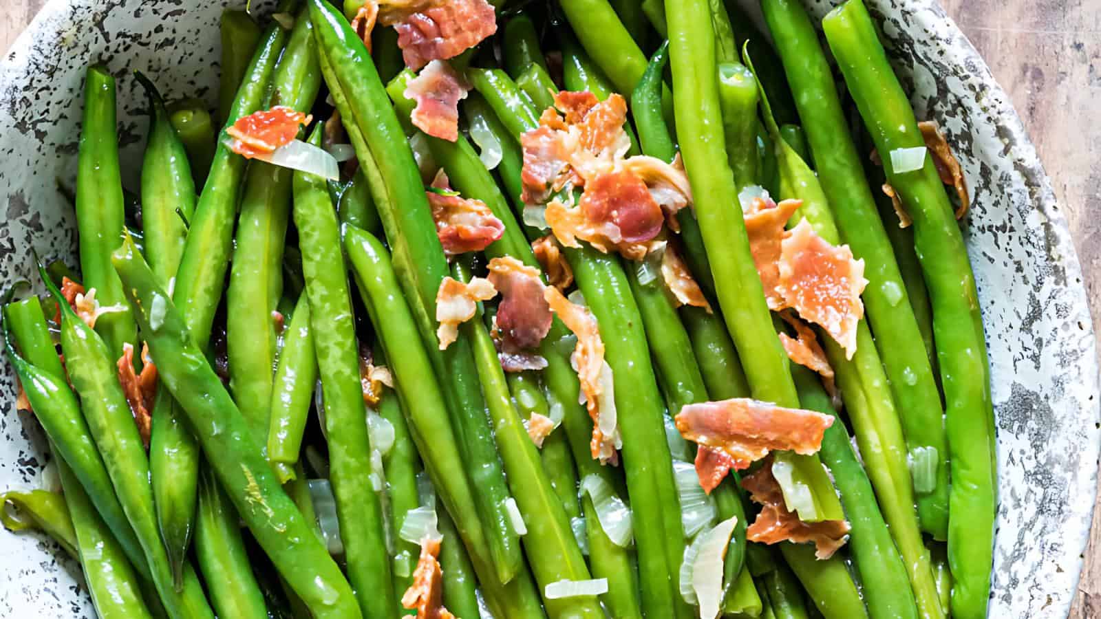 A plate with cooked green beans, crispy prosciutto pieces, and diced onions.