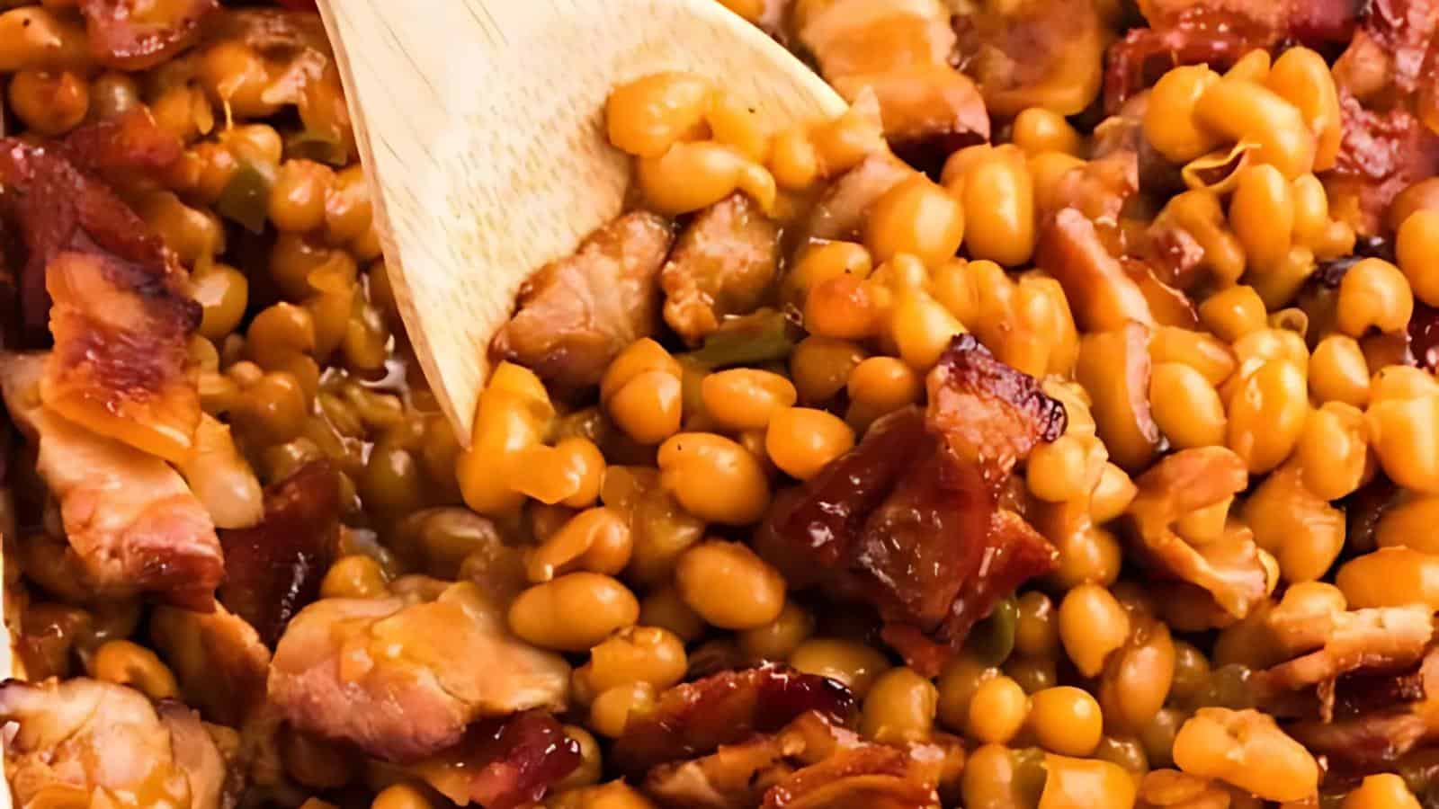 Baked beans mixed with pieces of bacon being stirred with a wooden spoon.