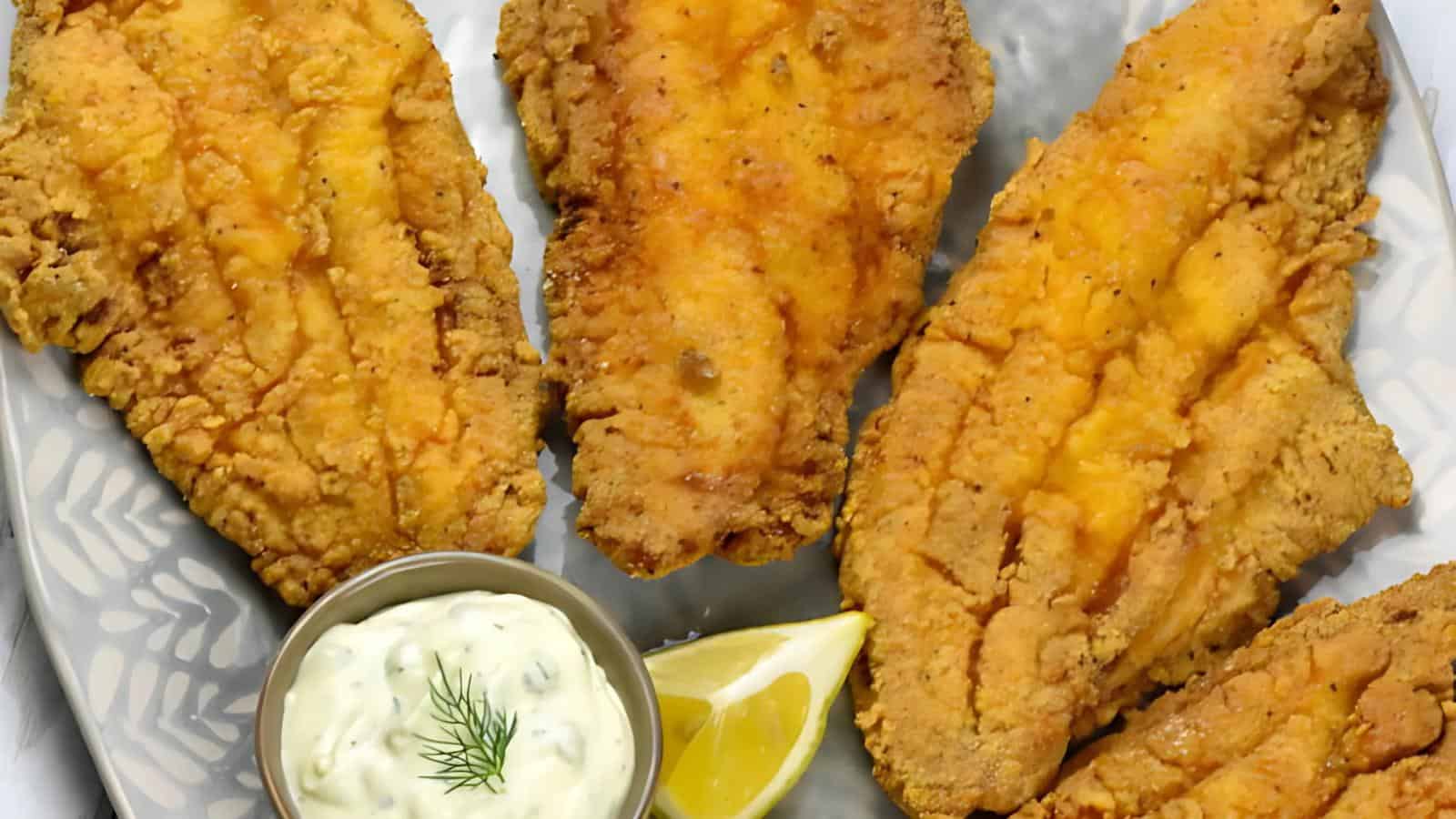 A plate containing four pieces of fried fish, a small bowl of tartar sauce, and a lemon wedge.