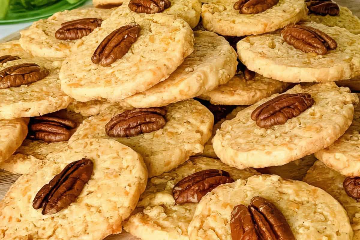 A pile of round cookies, each topped with a whole pecan half, arranged on a flat surface.