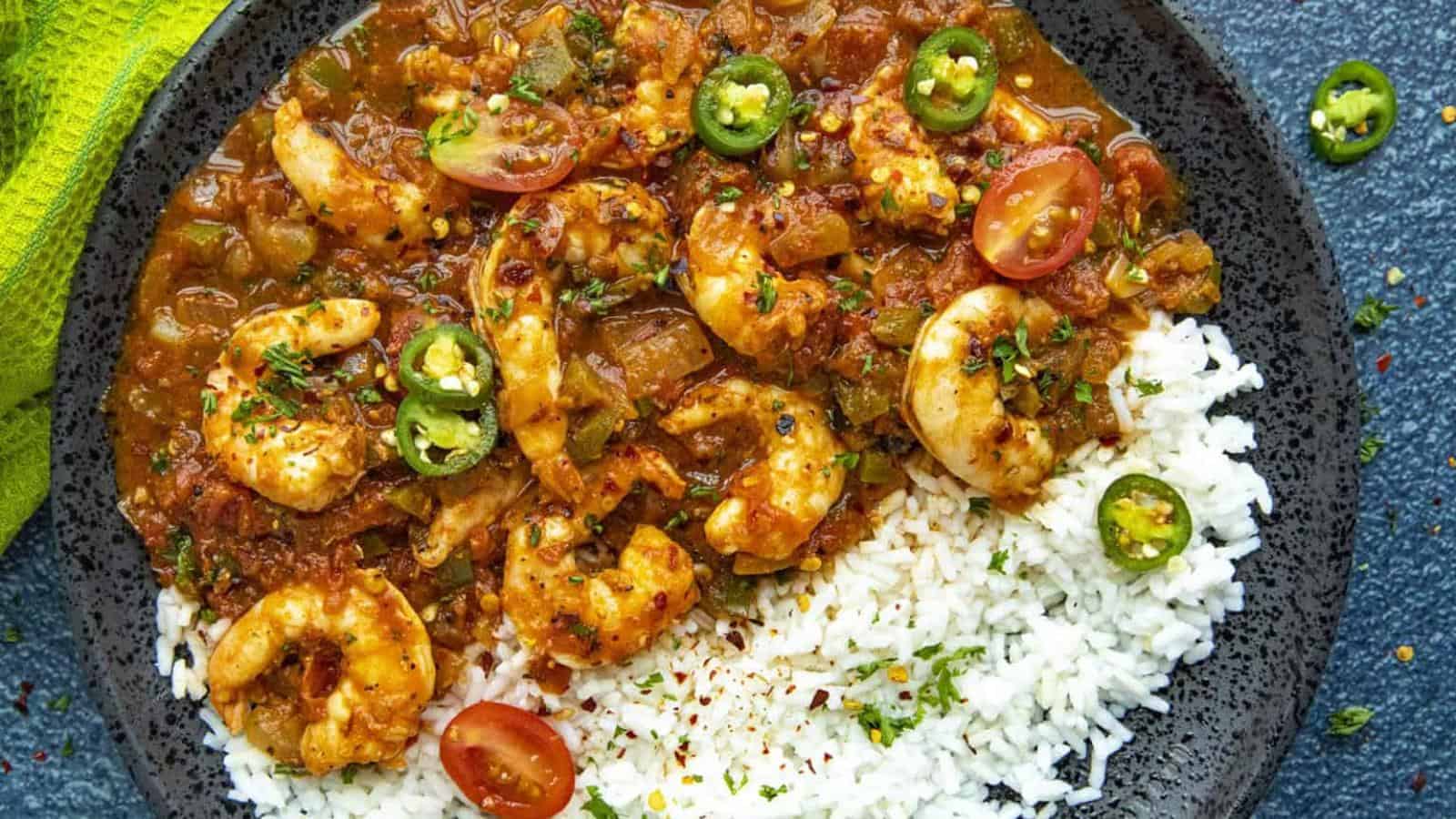 A dark dish featuring shrimp curry, white rice, sliced jalape&ntilde;os, and cherry tomatoes.