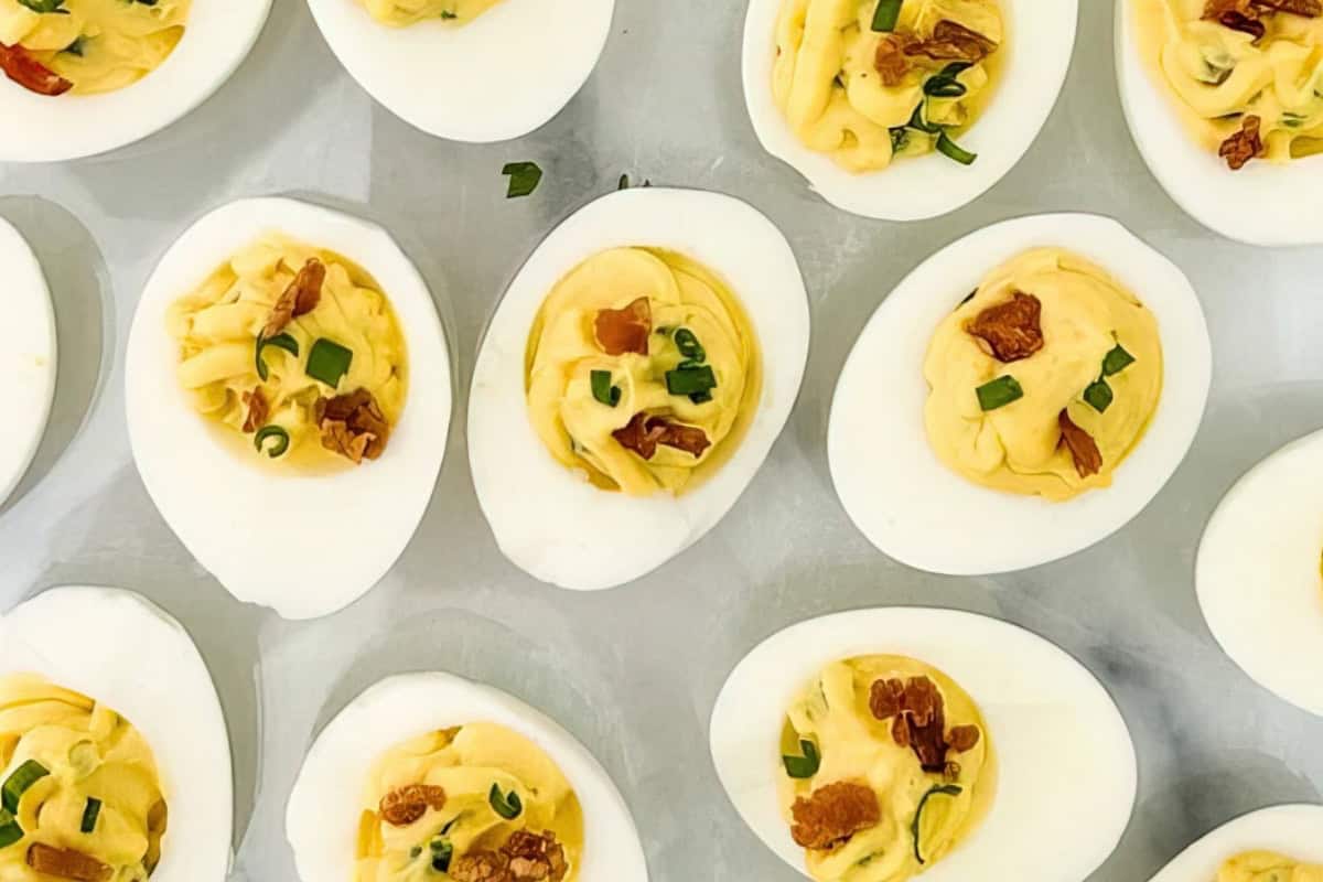A tray of deviled eggs topped with bacon bits and chopped green onions. The eggs are neatly arranged and have a creamy yellow filling.