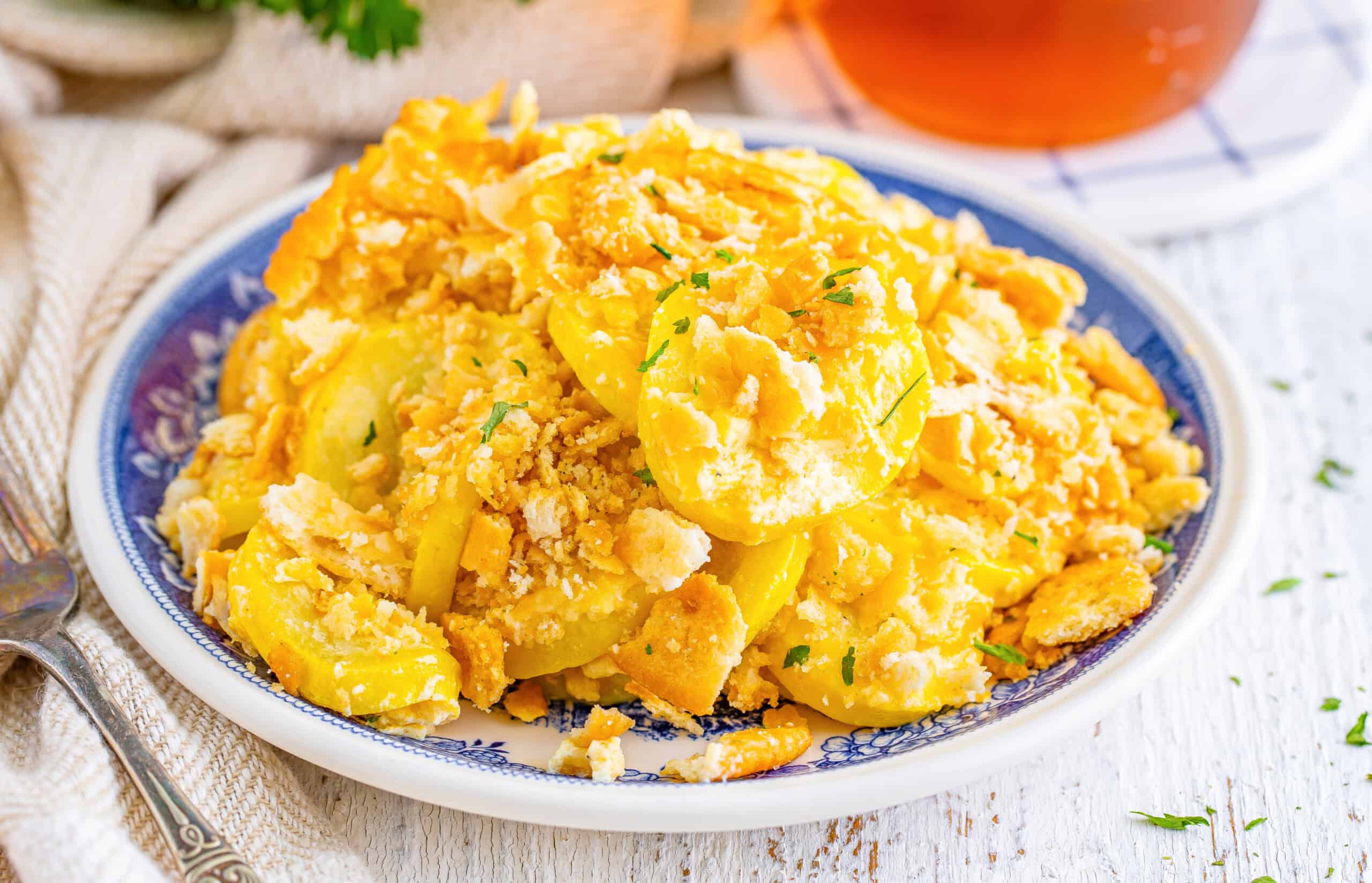 A plate of baked squash casserole topped with crumbled crackers and garnished with herbs on a blue-patterned dish.
