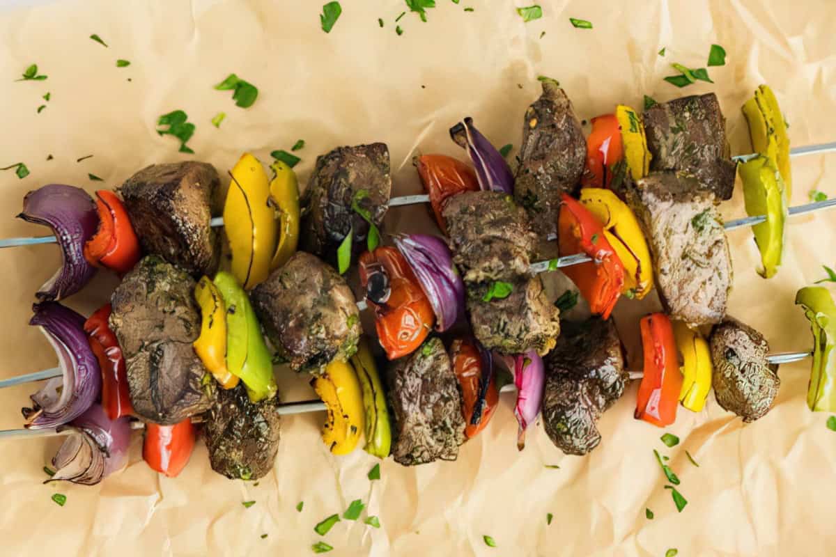 Grilled skewers with meat, red onion, cherry tomatoes, and bell peppers on parchment paper, garnished with chopped parsley.
