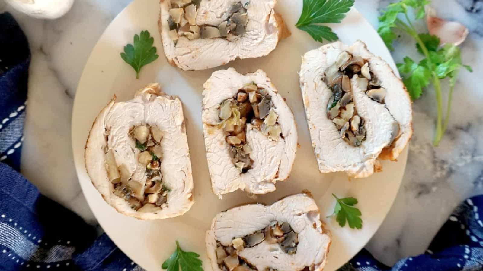 Sliced stuffed turkey breast on a white plate, filled with mushrooms and herbs, garnished with parsley.