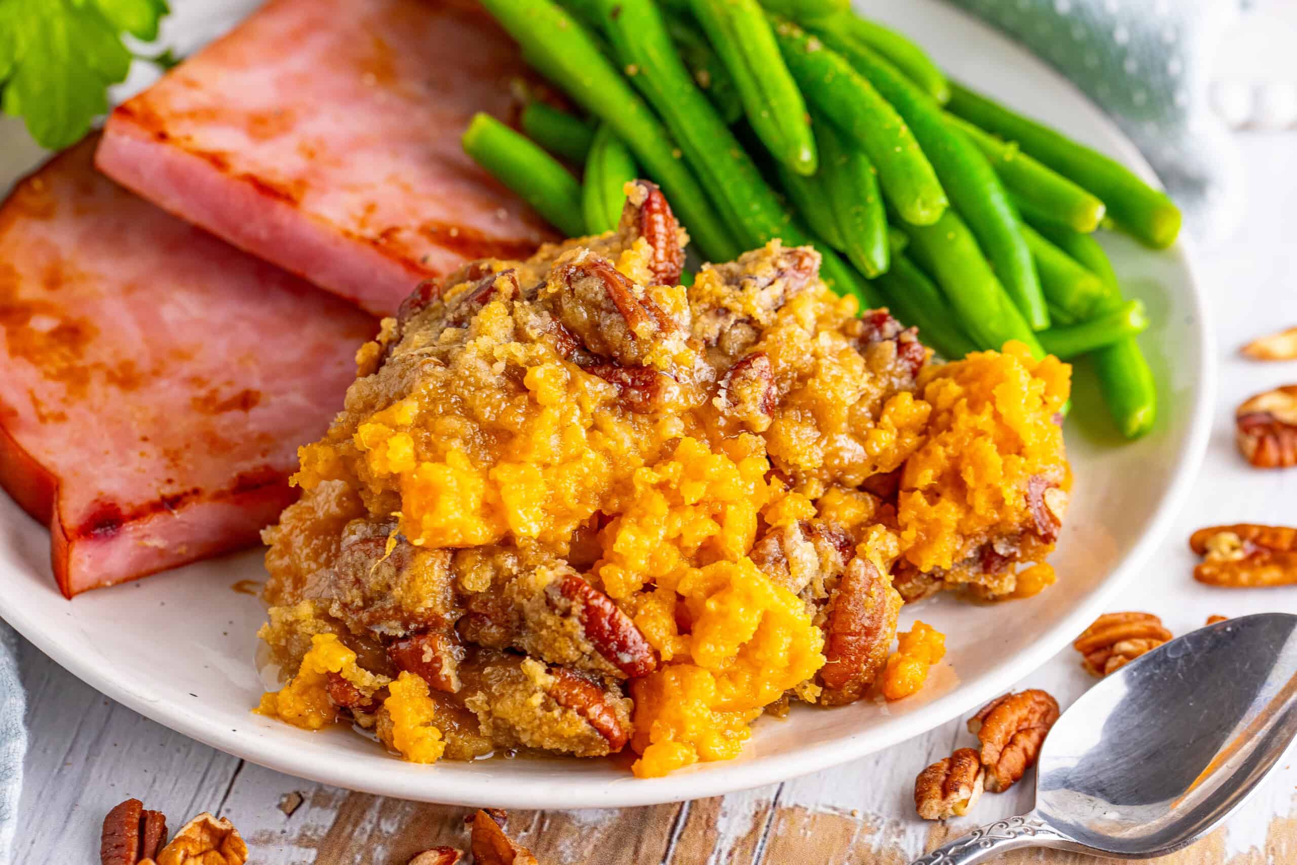The image depicts a plate featuring glazed ham, green beans, and sweet potato casserole topped with pecans.