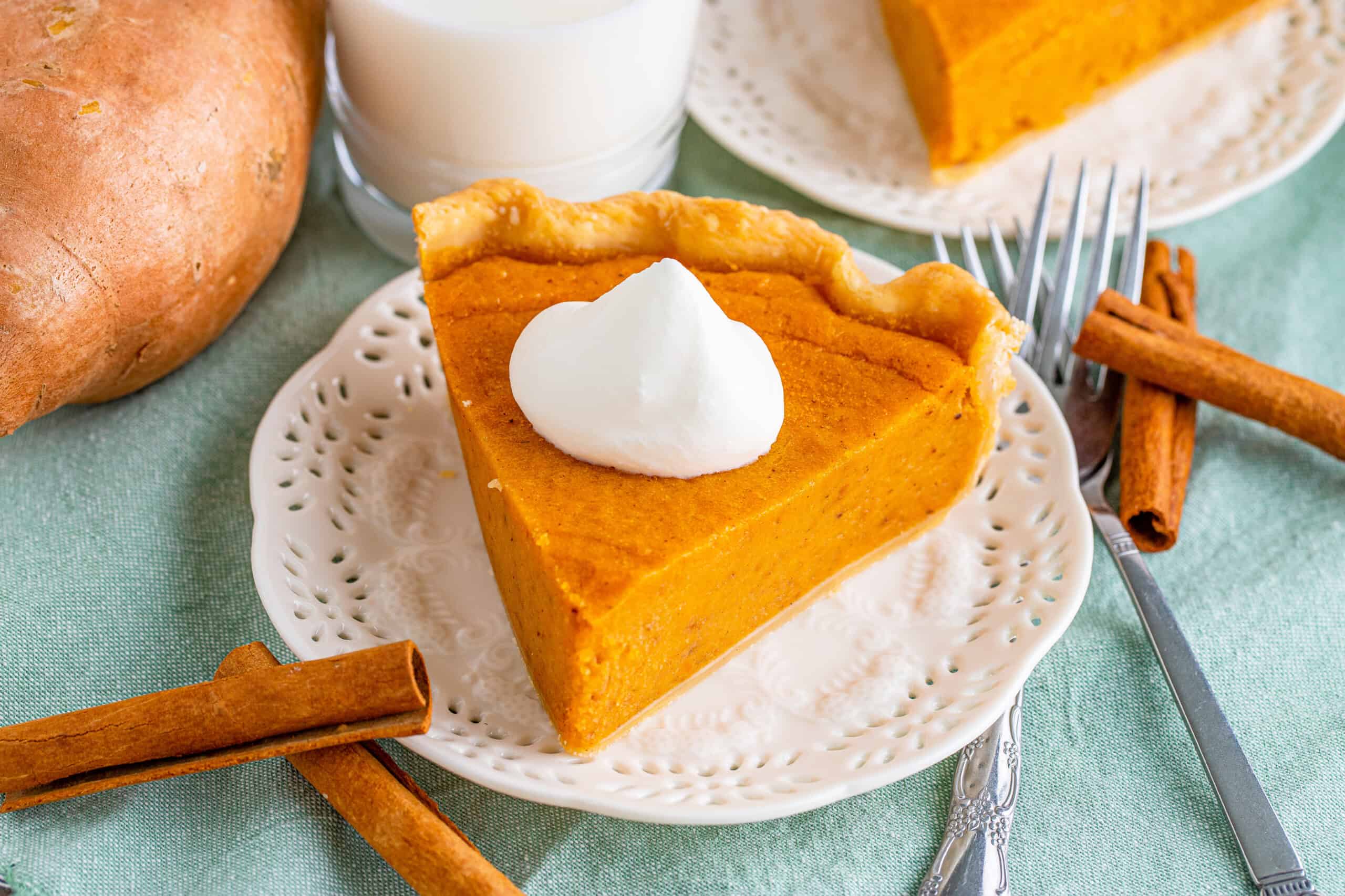 The image features a slice of pumpkin pie topped with whipped cream on a decorative plate, alongside cinnamon sticks and a fork. A glass of milk is visible in the background.