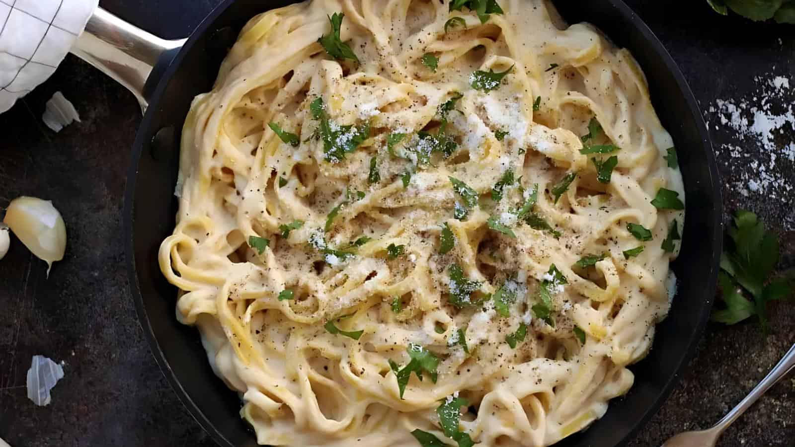 A skillet containing fettuccine pasta, parsley garnish, and grated cheese.