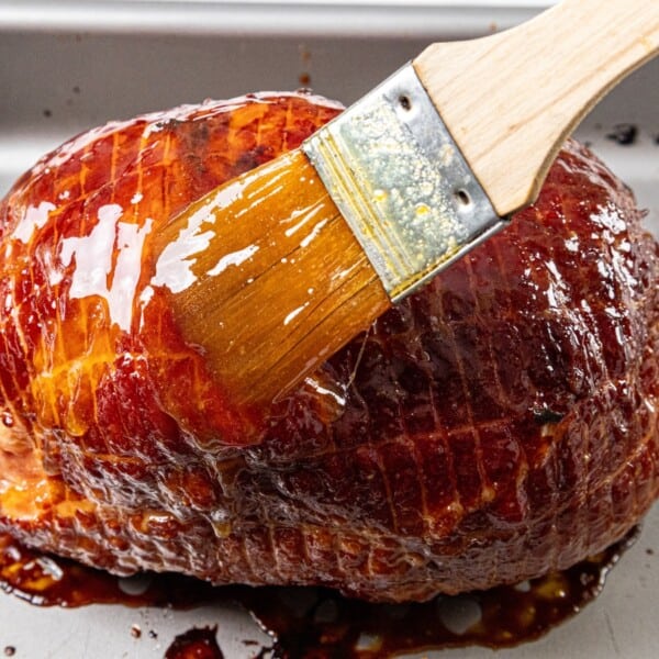 A metal roasting pan holds a baked ham covered with a glossy glaze.