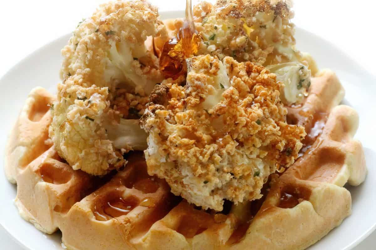 The image shows fried cauliflower on a waffle, drizzled with syrup, on a white plate.