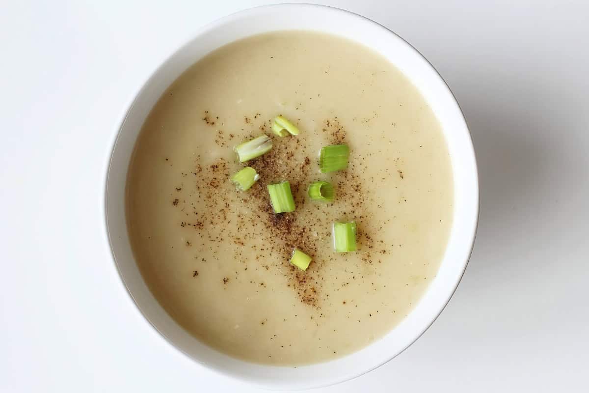 A bowl of soup with chopped green onions and ground pepper on top.