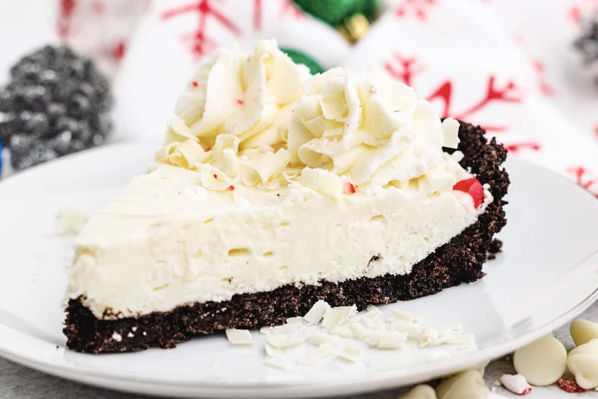 A slice of pie with a chocolate crust, a creamy filling, and whipped cream topping on a white plate.