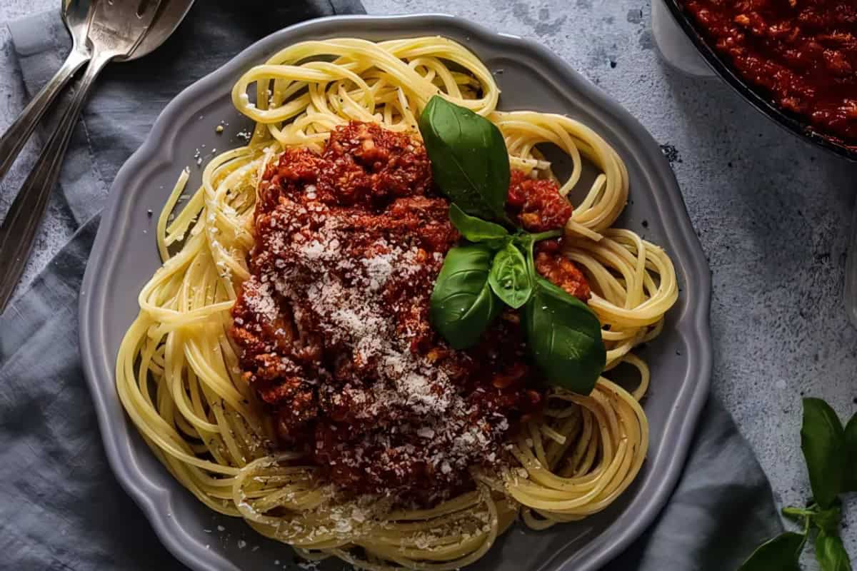A plate of spaghetti topped with tomato meat sauce, grated cheese, and fresh basil leaves.