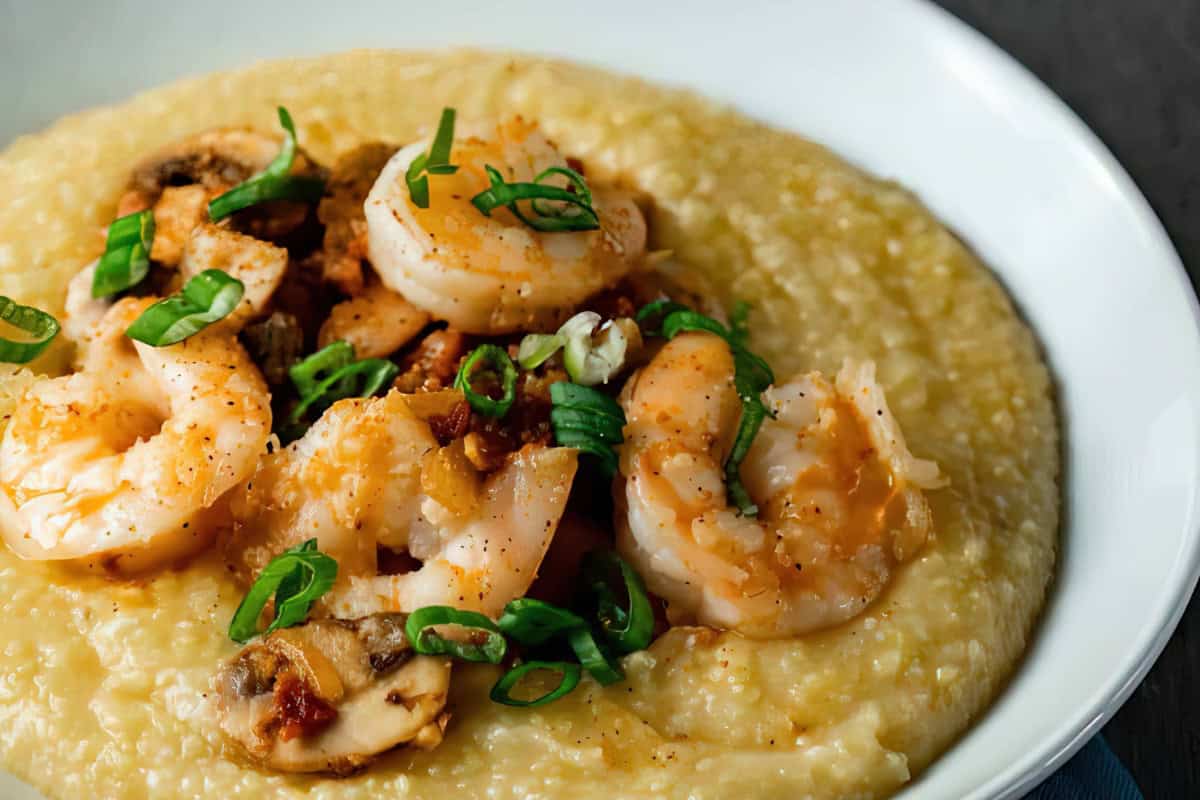 A bowl with grits topped with shrimp, mushrooms, bacon, and chopped green onions.