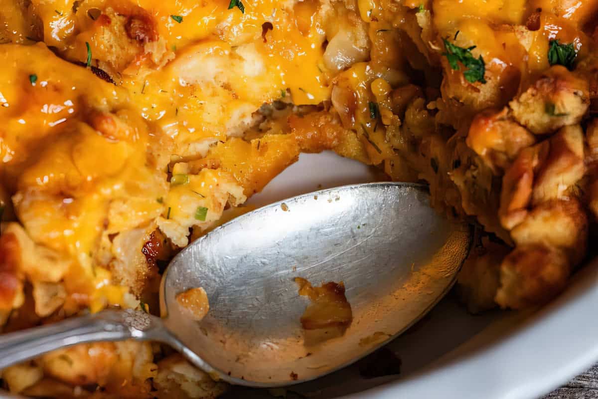 The image shows a white baking dish containing melted cheese and bread chunks, with a metal spoon partially scooping the contents.