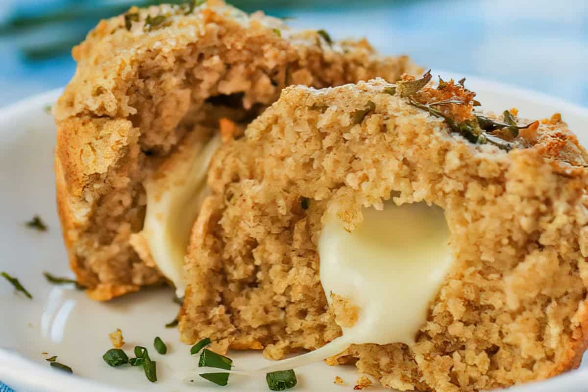 A stuffed muffin with melted cheese inside, garnished with herbs, on a white plate.
