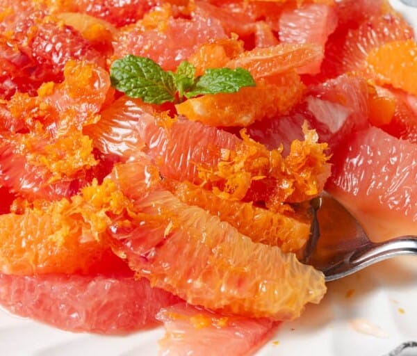 A plate of segmented grapefruit and orange, topped with orange zest and mint, with a spoon on the side.