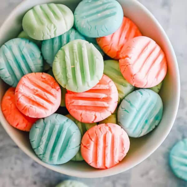 A bowl filled with round, pastel mint candies in light blue and pink, each topped with a ridged pattern.