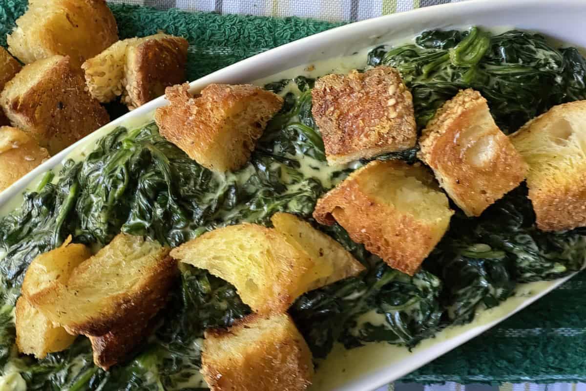 A white serving dish featuring creamed spinach topped with crispy croutons.